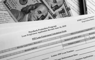A paycheck protection program (PPP) applications sits near US 100 dollar bills bearing Benjamin Franklin's face.
