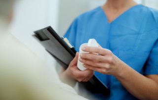 Nurse holding patient files handles bottle containing medication
